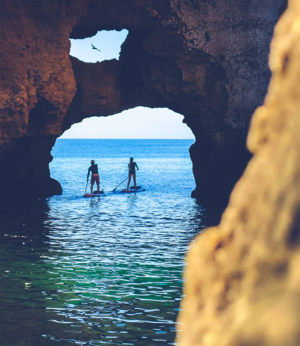 Un pareja haciendo Paddlesurf pasando por un arco de roca
